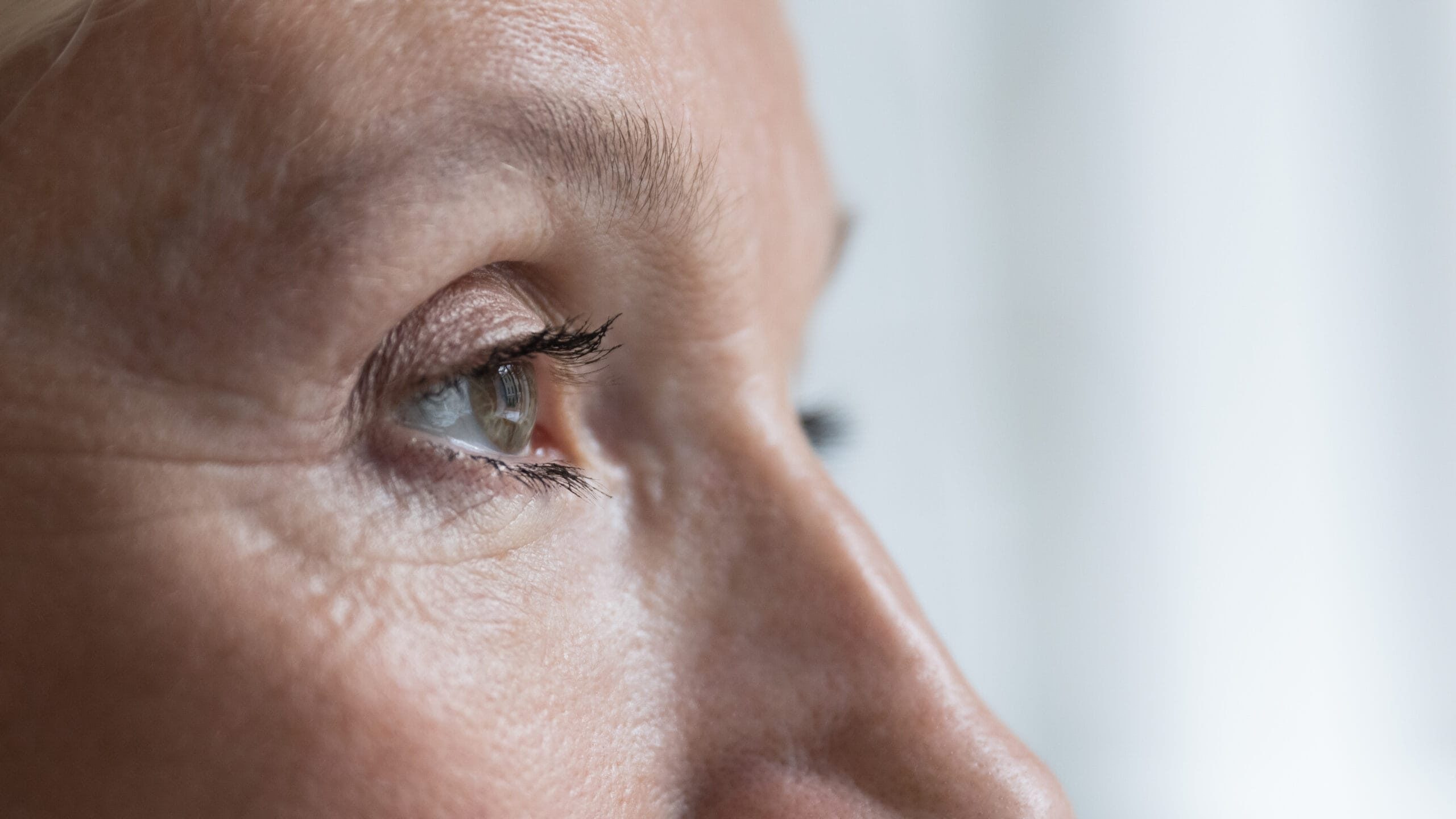 Close-up of an open eye with hazel iris and black eyelashes against neutral background
