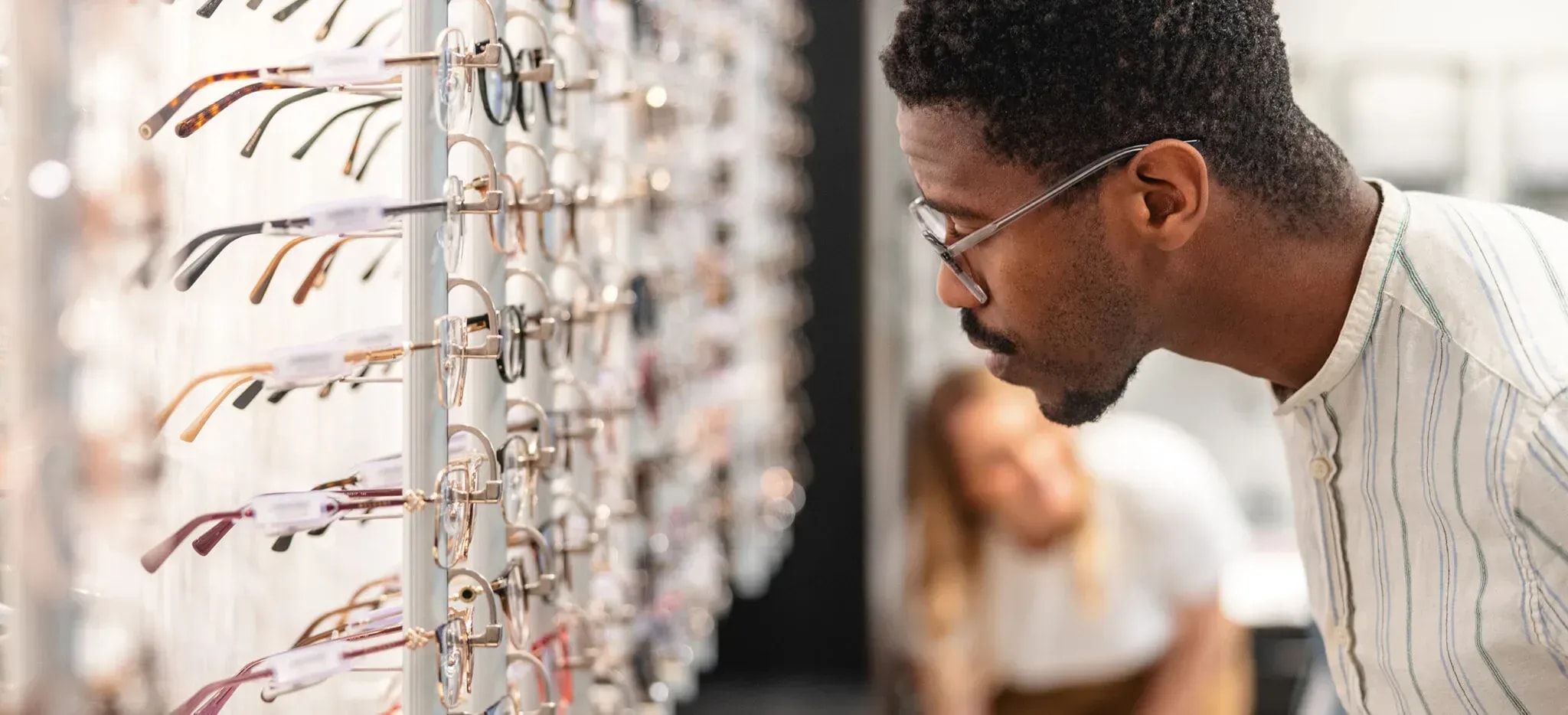 Man examining eyeglass frames from display wall at boutique optical shop
