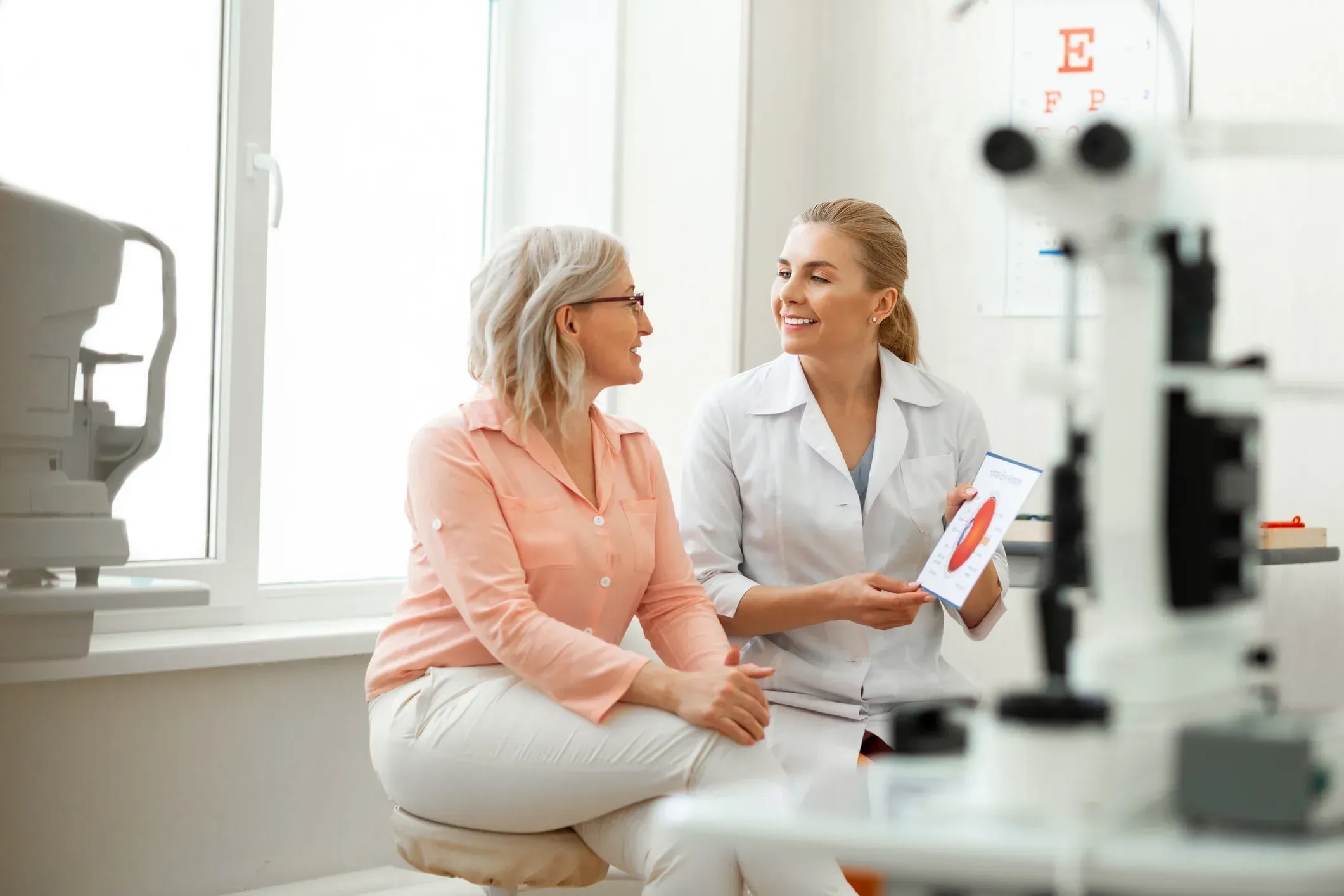 Optometrist and patient discussing eyewear in modern medical office with eye chart visible