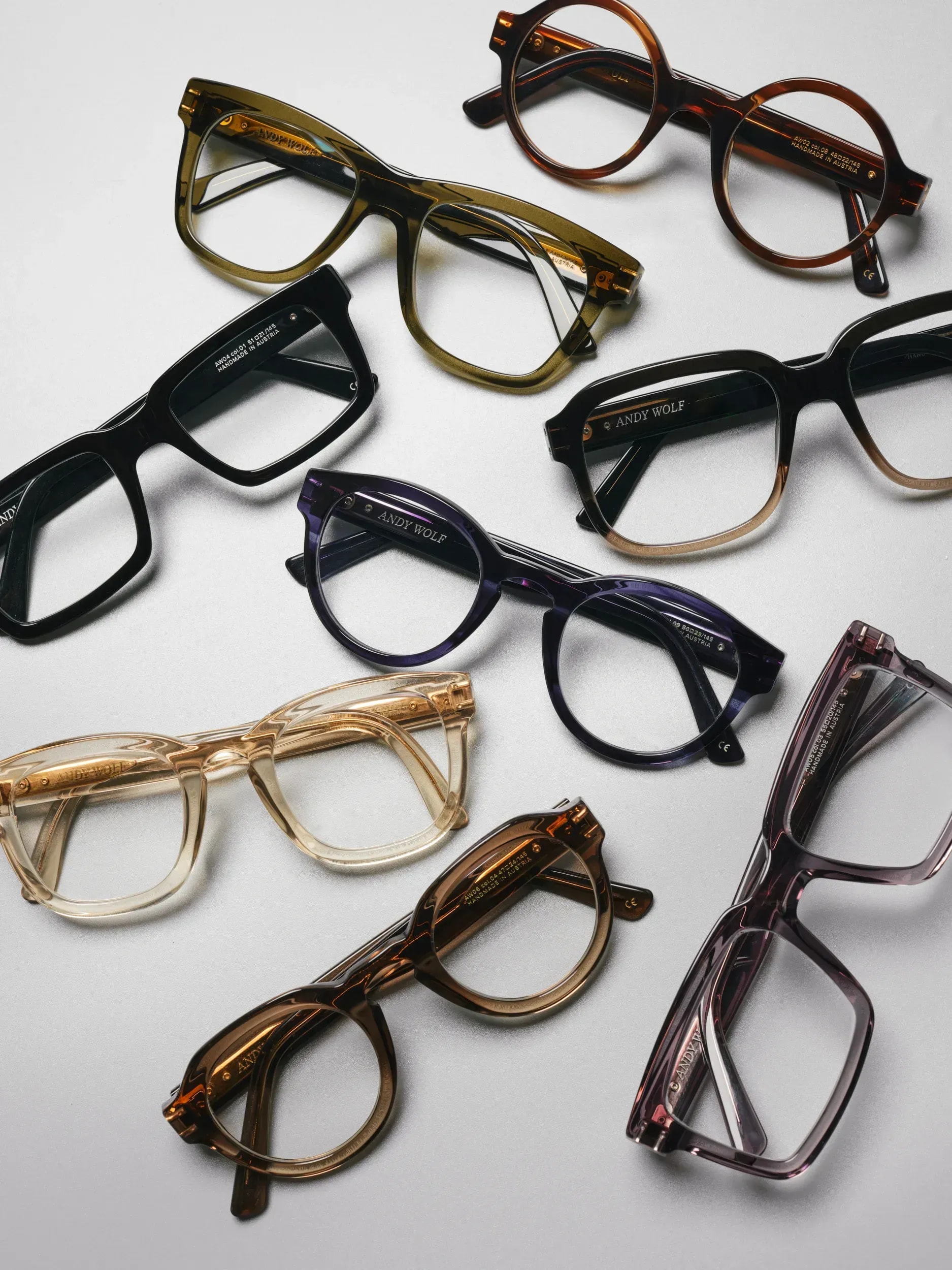 Nine pairs of eyeglasses in varied colors and styles arranged on white background.