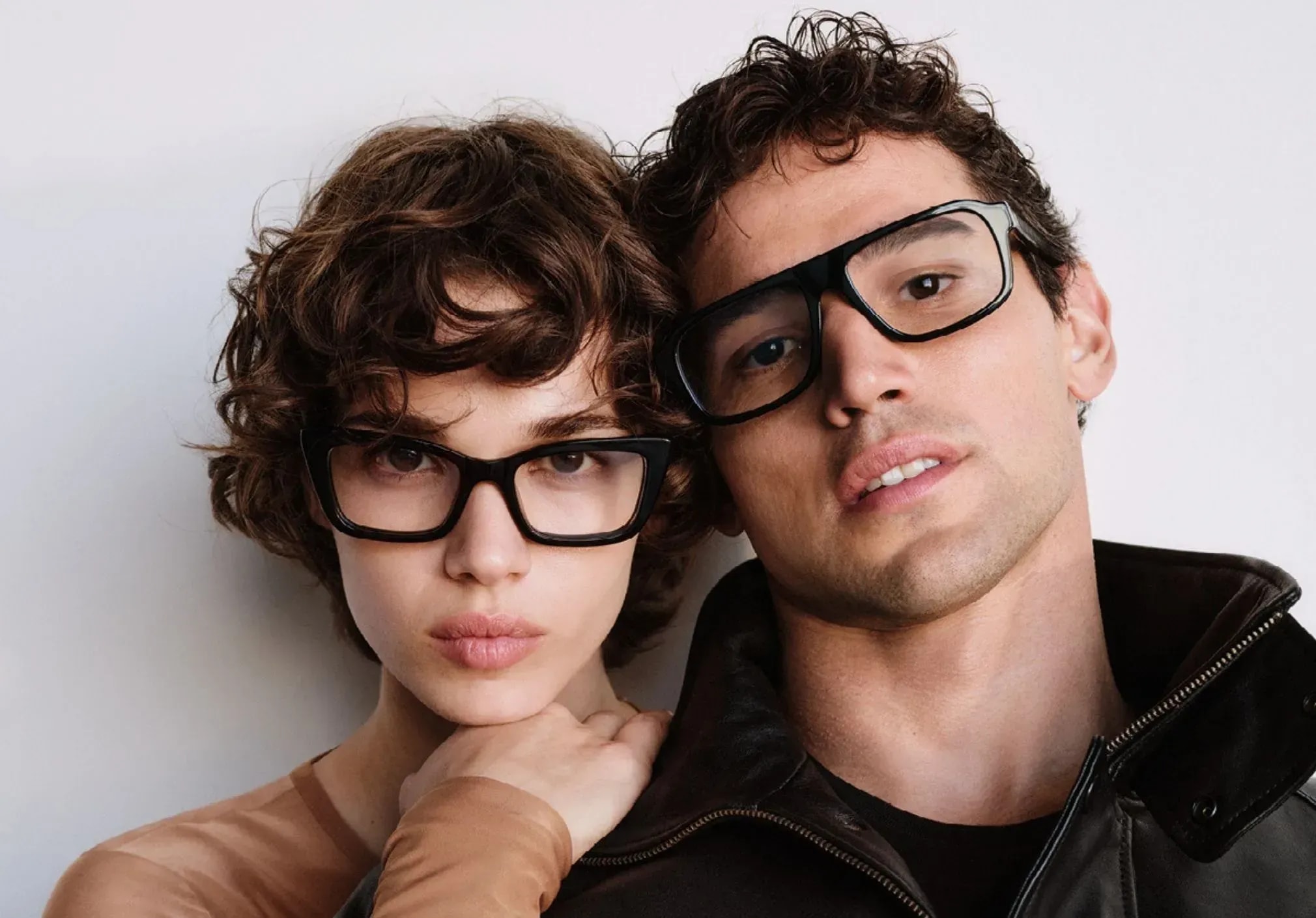 Two people wearing black-framed eyeglasses, posed together against a neutral background.