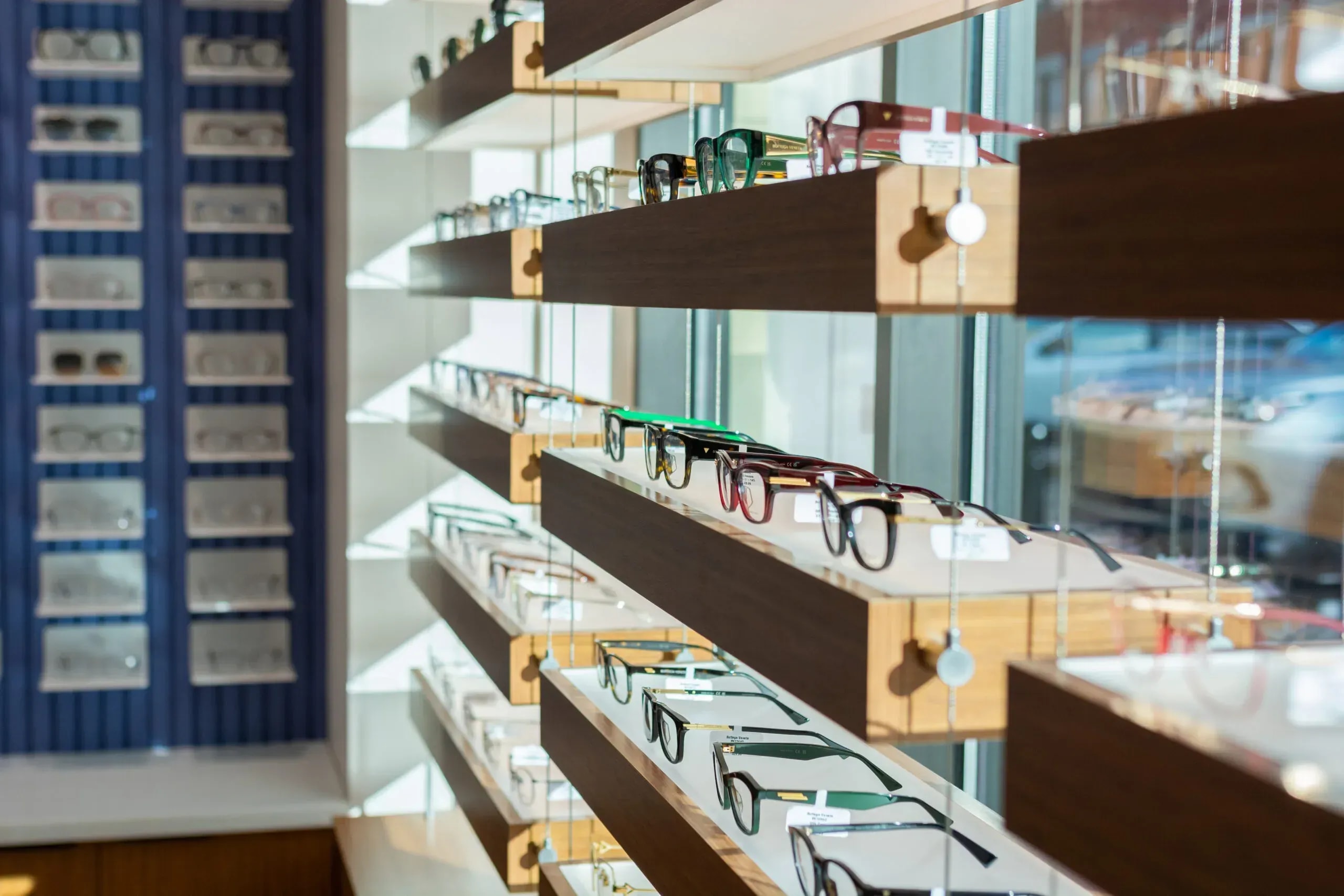Curated eyewear collection displayed on dark wood shelving in a bright retail space
