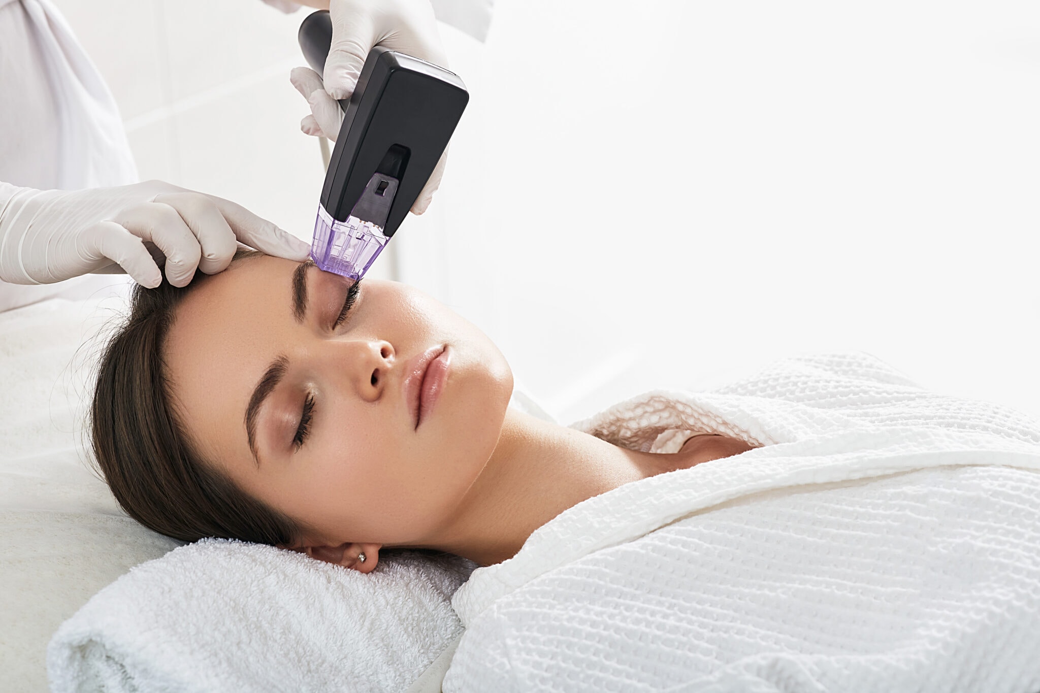 Aesthetic nurse practitioner administering RF microneedling treatment to patient's forehead
